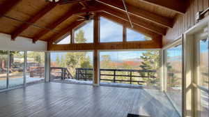Unfurnished sunroom with beam ceiling, ceiling fan, plenty of natural light, and a wooden deck