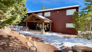 Snow covered back of property featuring stone siding and a patio area