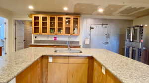 Kitchen with glass insert cabinets, light stone counters, recessed lighting, and light wood finish cabinets