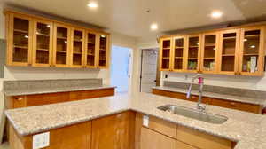 Kitchen featuring glass insert cabinets, light stone counters, recessed lighting, and light wood finish cabinetry