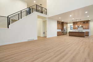 Unfurnished living room featuring recessed lighting, light wood-type flooring, and a high ceiling