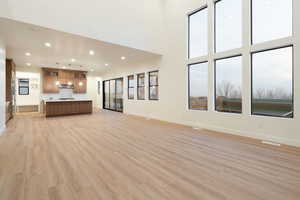 Unfurnished living room featuring light wood-type flooring, recessed lighting, and a high ceiling