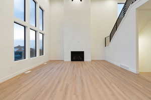 Unfurnished living room featuring plenty of natural light, a high ceiling, light wood-style flooring, and a fireplace