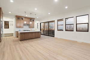 Kitchen featuring a kitchen island with sink, open floor plan, light countertops, wood finish cabinets, and light wood-type flooring
