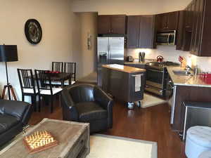 Kitchen with stainless steel appliances, dark wood-style flooring, dark wood finish cabinets, a center island, and open floor plan