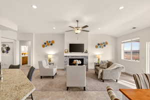 Living area featuring ceiling fan, a stone fireplace, light carpet, lofted ceiling, and recessed lighting