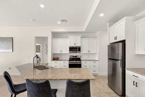 Kitchen featuring stainless steel appliances, light stone countertops, a breakfast bar, white cabinetry, and recessed lighting