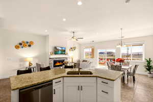 Kitchen with white cabinets, stainless steel dishwasher, a ceiling fan, a stone fireplace, and open floor plan