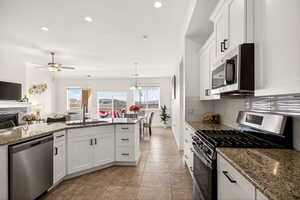 Kitchen featuring stainless steel appliances, white cabinetry, open floor plan, dark stone countertops, and light tile patterned floors