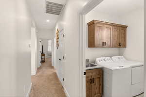 Laundry area with cabinet space, light colored carpet, washer and dryer, and recessed lighting