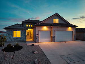 View of front of property featuring stone siding, stucco siding, an attached garage, and driveway