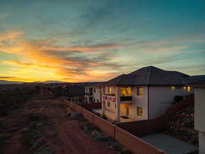 Back of house at dusk with a fenced backyard, stucco siding, and a balcony