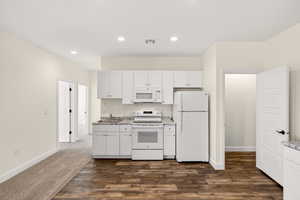 Kitchen featuring white appliances, dark wood-style floors, white cabinetry, recessed lighting, and light stone counters