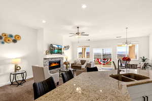 Kitchen featuring a ceiling fan, light stone counters, a chandelier, open floor plan, and a fireplace