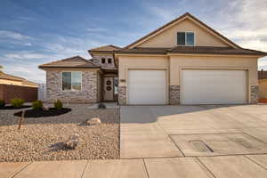 View of front of property with stucco siding, driveway, a tile roof, stone siding, and an attached garage