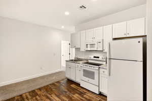 Kitchen featuring white appliances, dark wood-style flooring, white cabinets, and recessed lighting