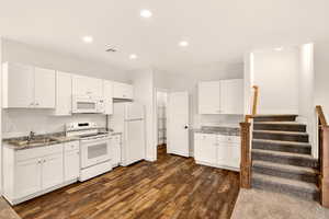 Kitchen featuring white appliances, white cabinetry, dark wood-type flooring, and recessed lighting