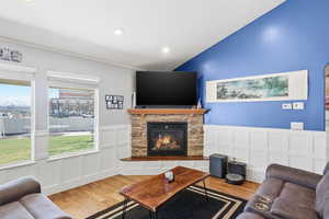 Living room featuring wood finished floors, wainscoting, a decorative wall, a stone fireplace, and recessed lighting