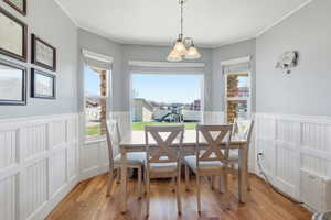 Dining space with light wood-style floors, healthy amount of natural light, ornamental molding, suspended lighting, and a wainscoted wall