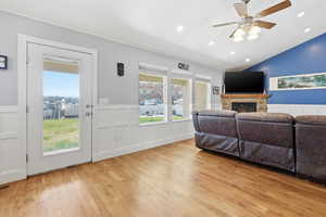 Living room with a wainscoted wall, a fireplace, light wood finished floors, ceiling fan, and plenty of natural light