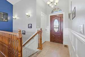 Entryway with a wainscoted wall, a decorative wall, suspended lighting, and light tile patterned flooring