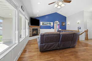 Living room featuring vaulted ceiling, light wood-style flooring, ceiling fan, a fireplace, and arched walkways