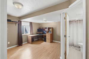 Home office with light wood-style flooring and a textured ceiling