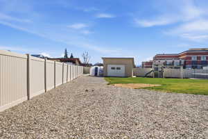 Fenced backyard with a playground, an outdoor structure, gravel driveway, and a detached garage