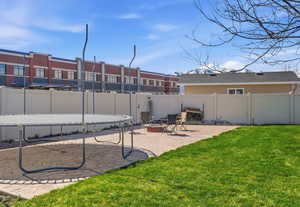 Fenced backyard with a patio area, a trampoline, and an outdoor fire pit