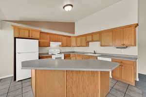 Kitchen with white appliances, a kitchen island, light tile patterned flooring, vaulted ceiling, and light countertops