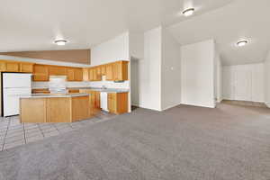 Kitchen with vaulted ceiling, white appliances, open floor plan, light colored carpet, and light countertops