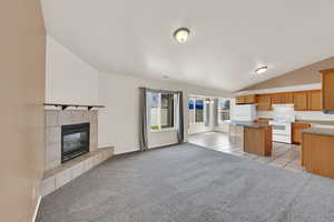 Kitchen with open floor plan, a kitchen island, white appliances, vaulted ceiling, and light colored carpet