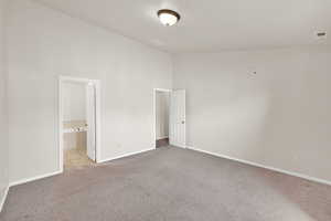 Unfurnished bedroom with carpet, ensuite bathroom, and a high ceiling