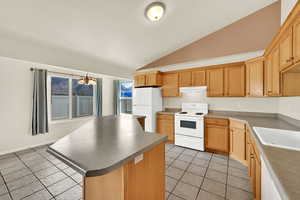 Kitchen featuring white appliances, a center island, vaulted ceiling, light tile patterned flooring, and light wood finish cabinetry