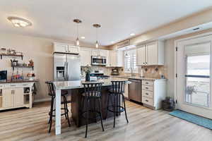 Kitchen featuring light stone countertops, two tone color scheme, a center island, a breakfast bar, and light wood-style flooring