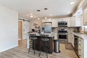 Kitchen featuring a barn door, stainless steel appliances, a kitchen island, light stone counters, and two tone cabinets