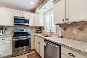 Kitchen with stainless steel appliances, pendant lighting, light stone countertops, light wood-type flooring, and white cabinets
