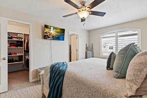 Bedroom featuring a spacious closet, a textured ceiling, a ceiling fan, and light colored carpet