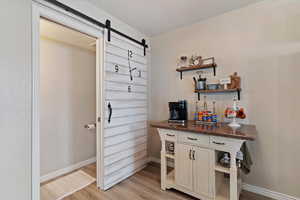 Bar area featuring a barn door, dark stone counters, open shelves, and light wood-type flooring