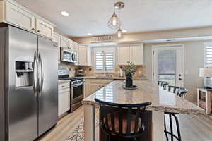 Kitchen with stainless steel appliances, a breakfast bar area, light wood-style flooring, a kitchen island, and light stone countertops