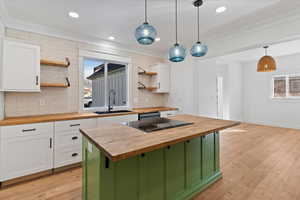 Kitchen featuring butcher block counters, light wood-style flooring, decorative backsplash, and crown molding