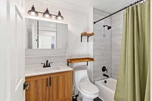 Bathroom with wallpapered walls, shower / bath combo with shower curtain, and vanity
