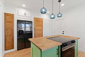 Kitchen with butcher block countertops, black appliances, green cabinets, light wood-style floors, and ornamental molding