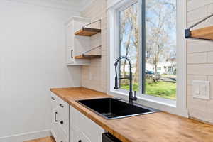 Kitchen with white cabinets, open shelves, ornamental molding, butcher block counters, and light wood-style floors