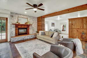 Living room featuring a fireplace, ceiling fan, and stone tile floors
