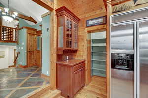 Kitchen featuring stainless steel built in fridge, a chandelier, glass insert cabinets, light countertops, and inlaid floor details