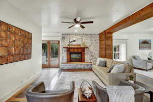 Living room with a stone fireplace, beamed ceiling, ceiling fan, and french doors