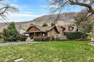 View of front facade featuring a porch, a front lawn, a mountain view, a chimney, and stone siding