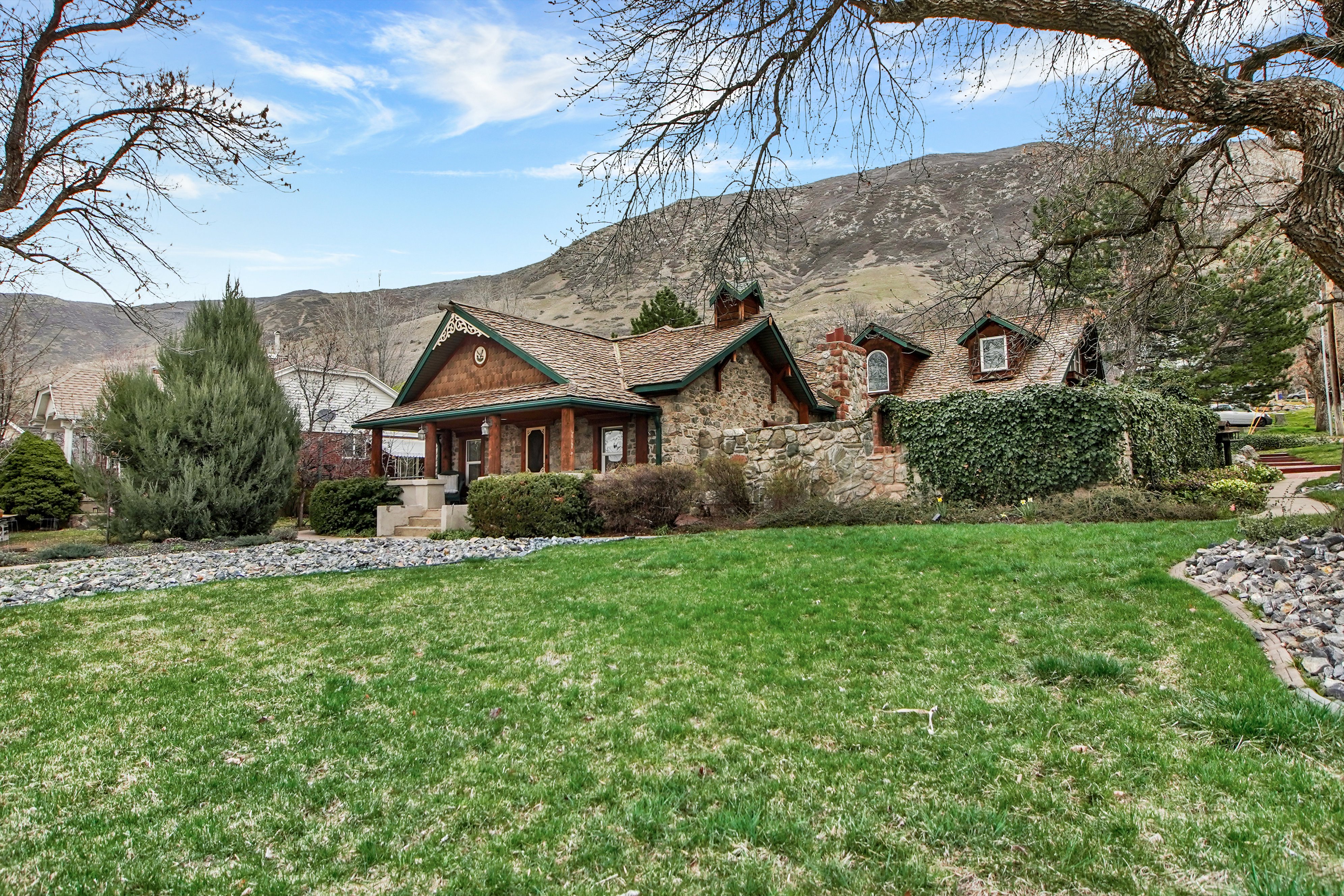 View of front of house featuring a porch, a front yard, a chimney, a mountain view, and stone siding