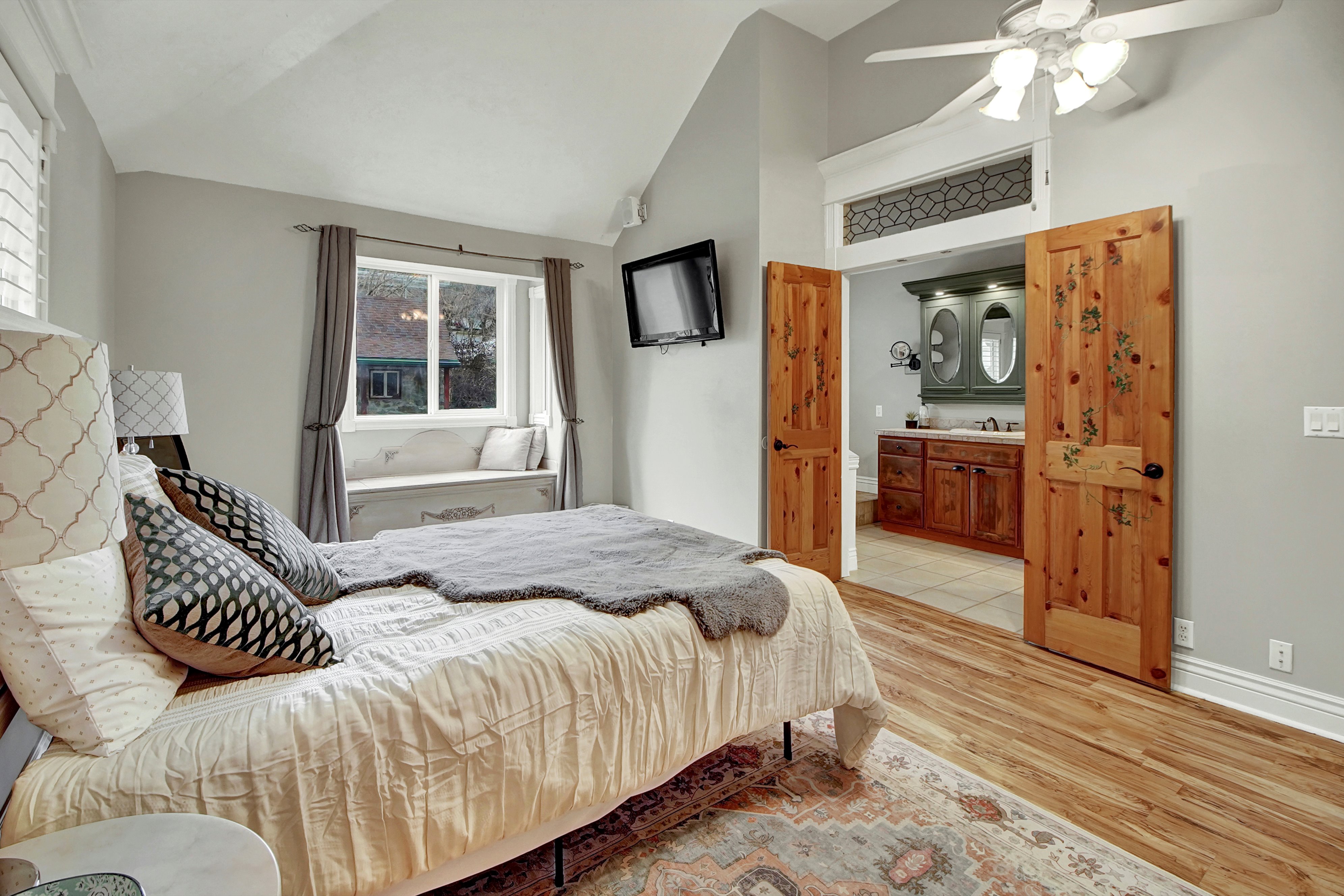 Bedroom with light wood-style flooring, vaulted ceiling, ceiling fan, and ensuite bath